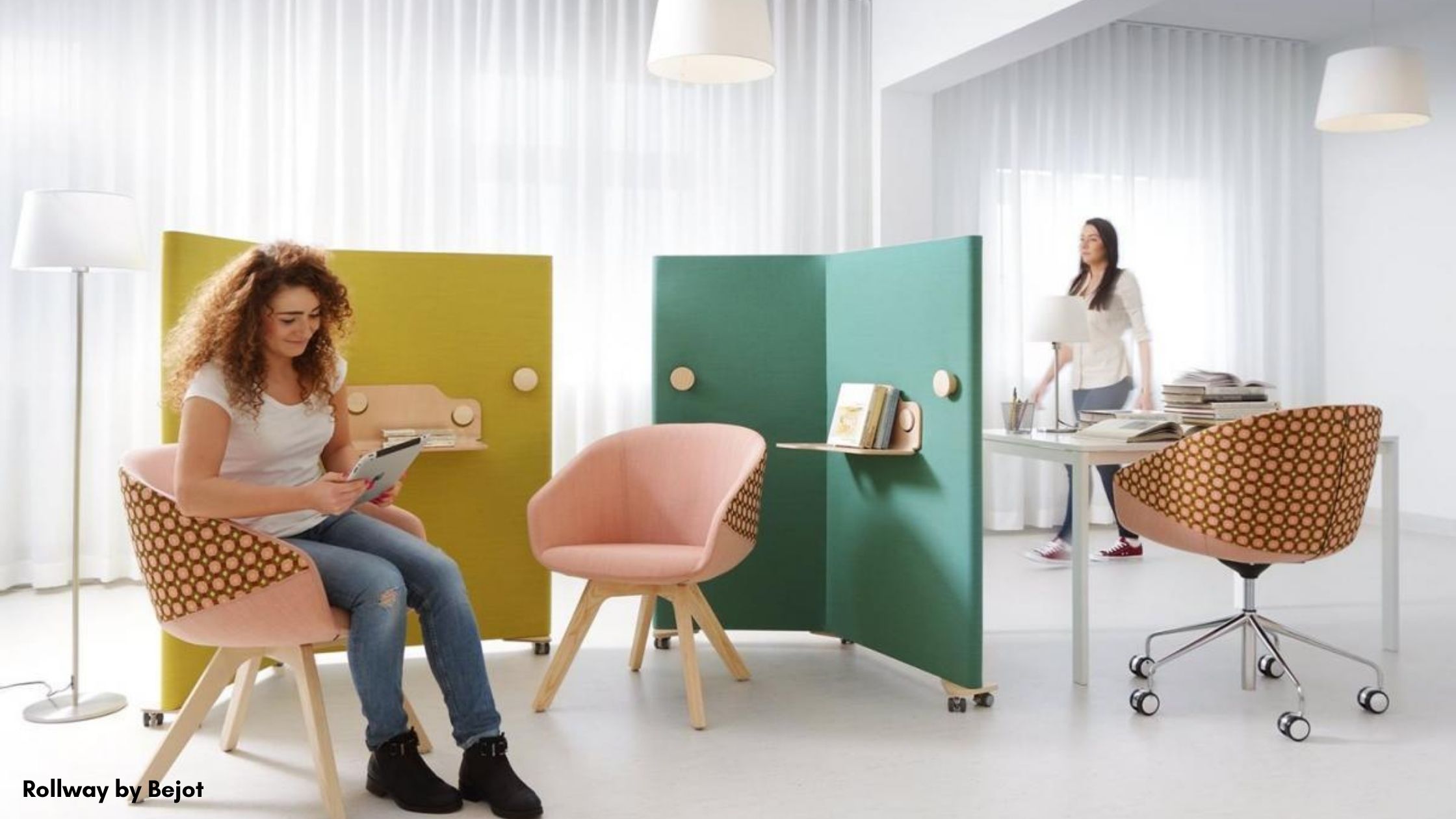 Woman sitting on a chair in an office in front of yellow and teal acoustic separators on wheels